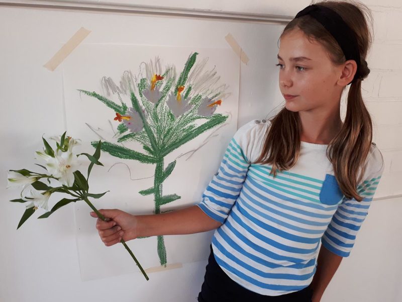 Child standing with drawing of flowers and a bunch of flowers