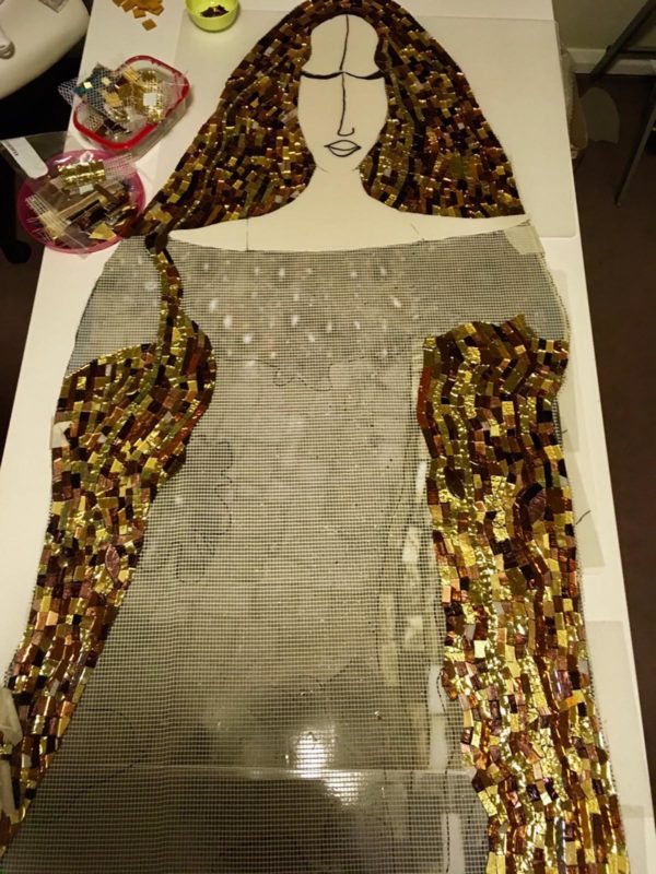 In progress mosaic of woman in gold and brown.