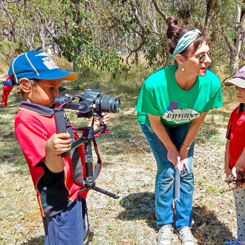 Woman in green standing with two children operating a camera