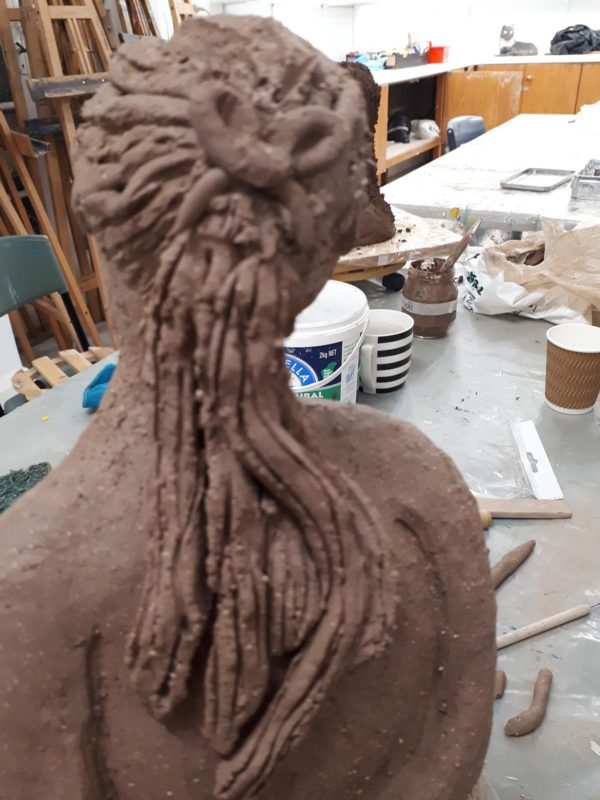Rear view of a brown clay sculpture of a woman's head in workshop