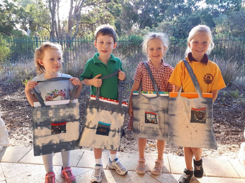 Children standing with tie-dye tote bags