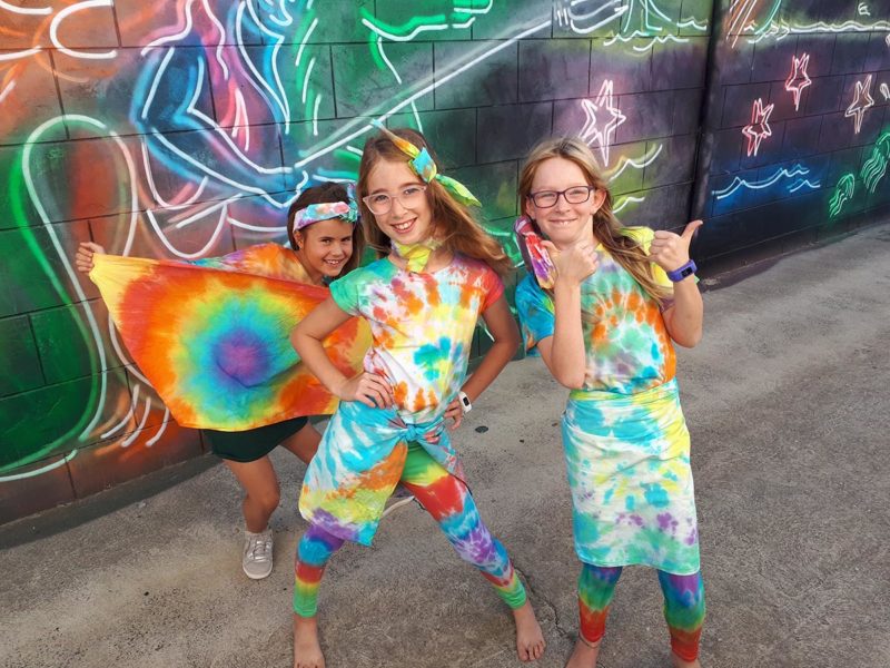 Children dressed in tie-dye clothing in front of feature wall